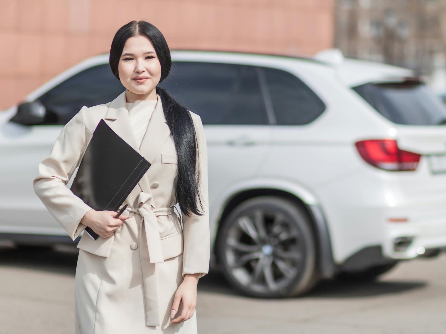 A professional smiling insurance agent showing a car insurance policy to a happy couple with a car in the background